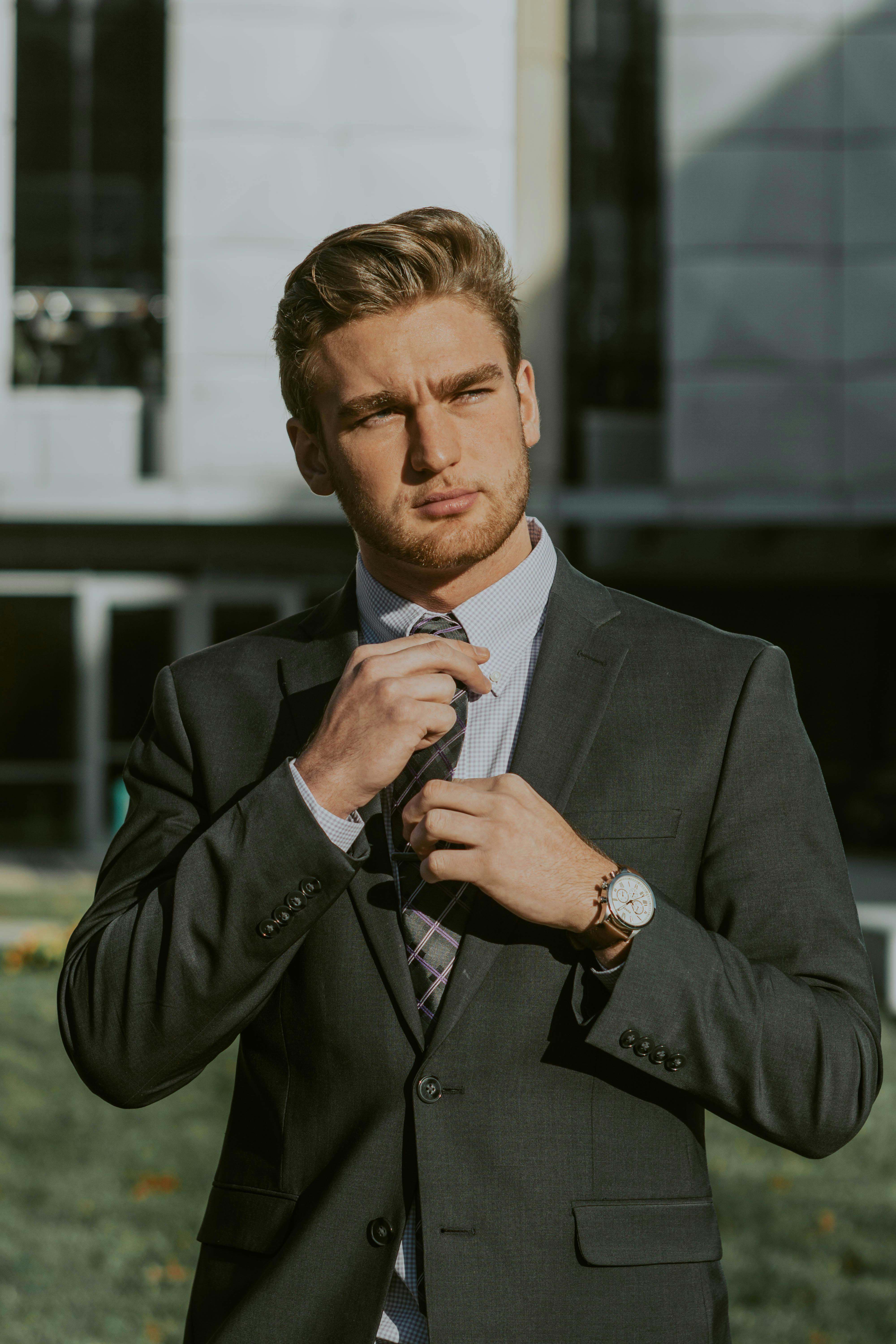 Confident young professional adjusting his tie, standing in front of a modern office building.